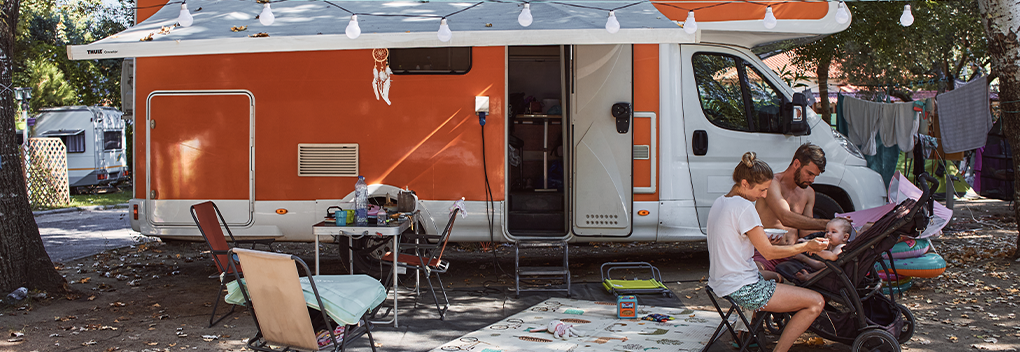 Family of three sitting outside eating and camping with their RV.